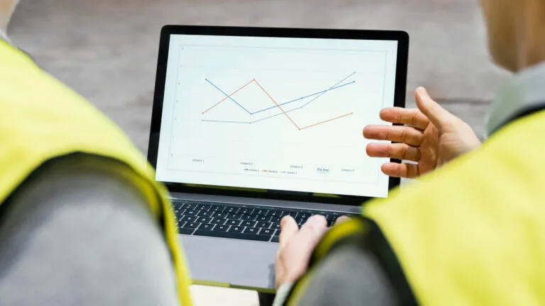 Maturidade de Marketing Industrial: duas pessoas com colete de segurança analisando um notebook com gráficos.